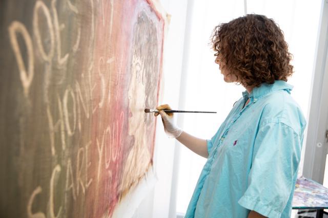 A student wearing a light blue collard shirt paints a face on a canvas