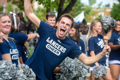 A student wearing a Longwood Cheer tshirt smiles at the camera.