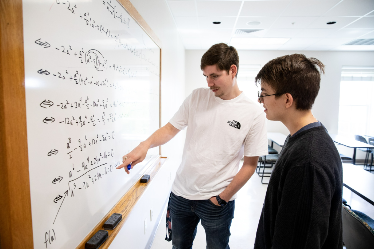 Brandon Walters '23 (pictured left) with Nicolas Freeman '25 (pictured right) stand at a white board that shows their research.