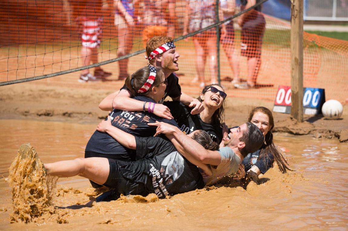 Longwood students collapse in a pile, laughing, during a game of volleyball in the mud