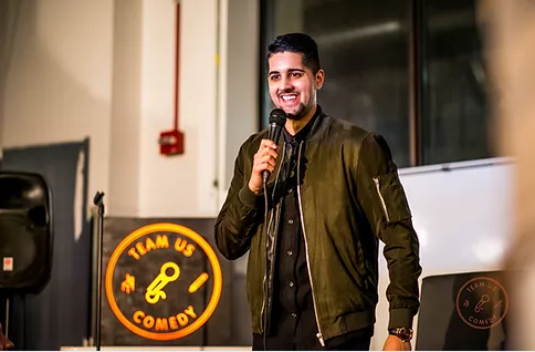 Comedian Vik Pandya stands holding microphone.
