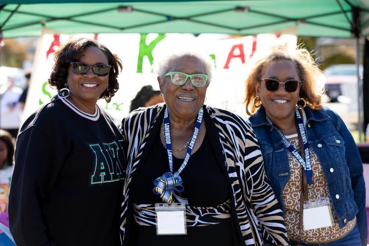 Three Black Longwood alumnae smile together at Homecoming.