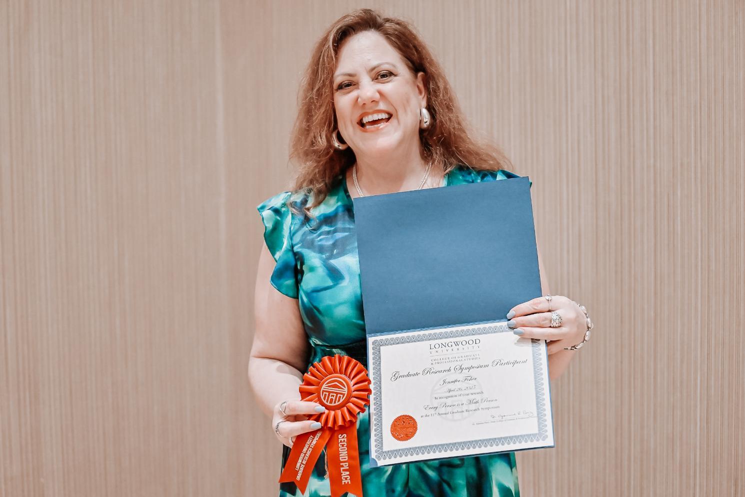 Fisher - A person holds a certificate and a red “SECOND PLACE” ribbon from Longwood.   The certificate recognizes participation in the Graduate Research Symposium.   They wear a blue-green patterned outfit and are smiling.   The setting reflects academic achievement and recognition.