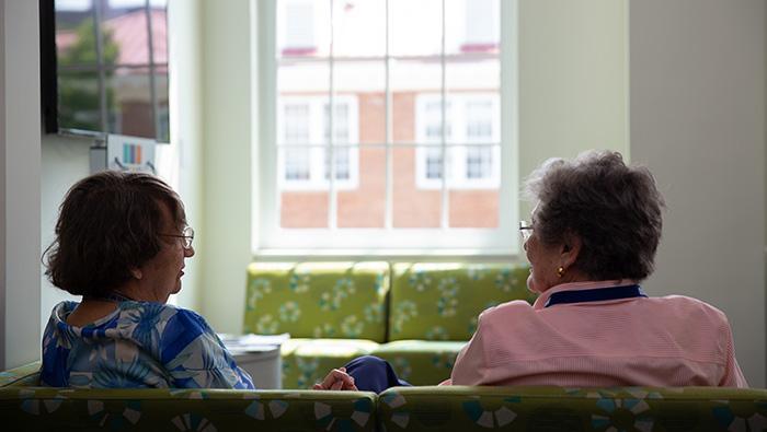 The backs of heads of two people chatting on a couch with a window in front