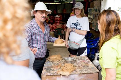 Man in a white hat holds up a small clay sculpture on a board.