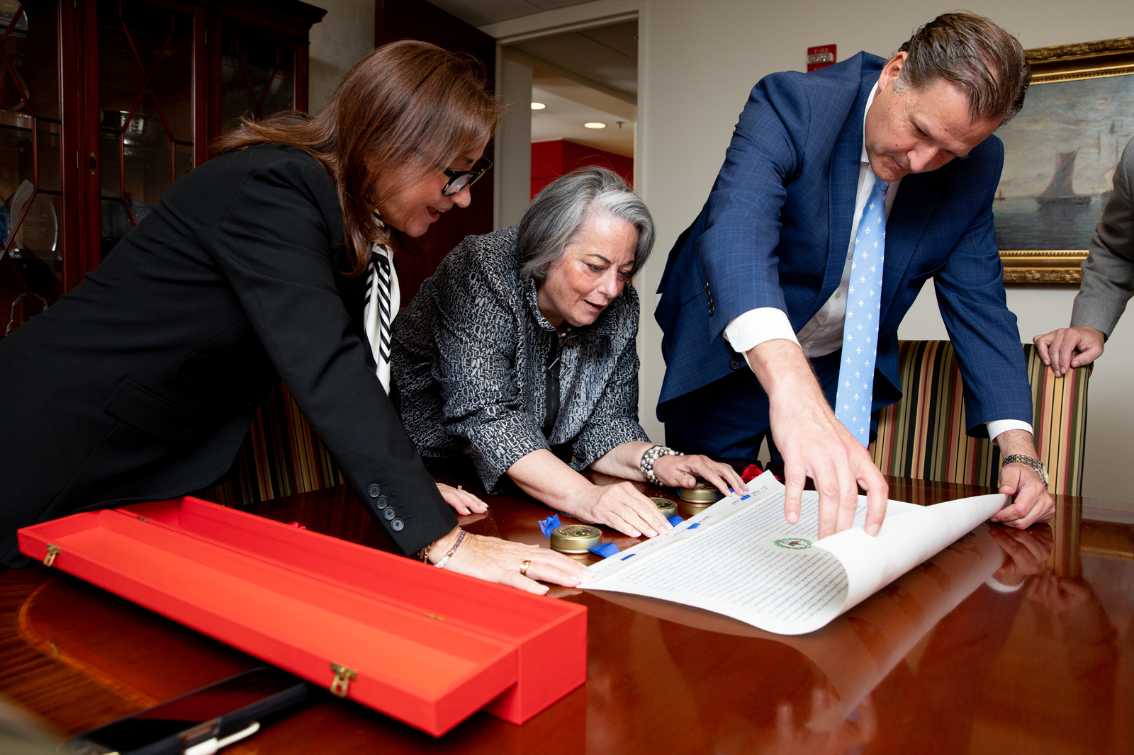 Marianne Radcliff '92, Pia Trigiani and President W. Taylor Reveley IV examine Longwood’s hand-drawn letter of patent in Trigiani’s Alexandria office, following its presentation at the British Embassy in Washington, D.C.