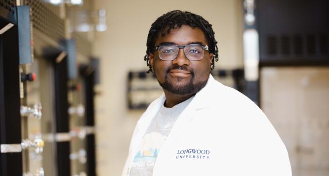 Antonio Harvey ’25 - A student wearing a white lab coat embroidered with “Longwood University” stands in a science laboratory. He faces the camera with a confident, relaxed expression. Glassware and lab equipment line the benches behind him. The setting suggests a chemistry lab environment.