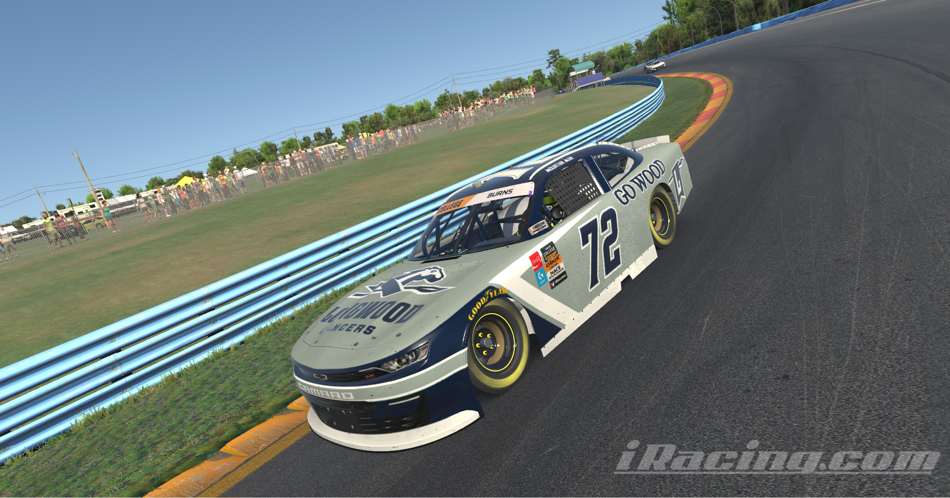 No. 72 Longwood Lancers Chevrolet Camaro - Longwood Lancers–branded No. 72 stock car races along a curved track. The car features “Goodwood” sponsorship and Goodyear tires. Blue guardrails line the course with spectators behind a fence. The image appears to be a racing simulation screenshot.