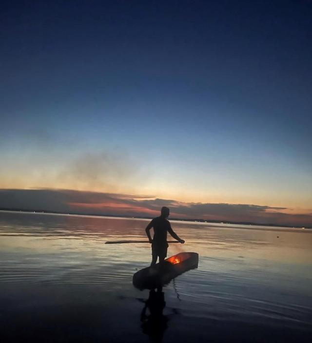 Russell Reed in one of his canoes, paddling through water with a colorful sunset in the background