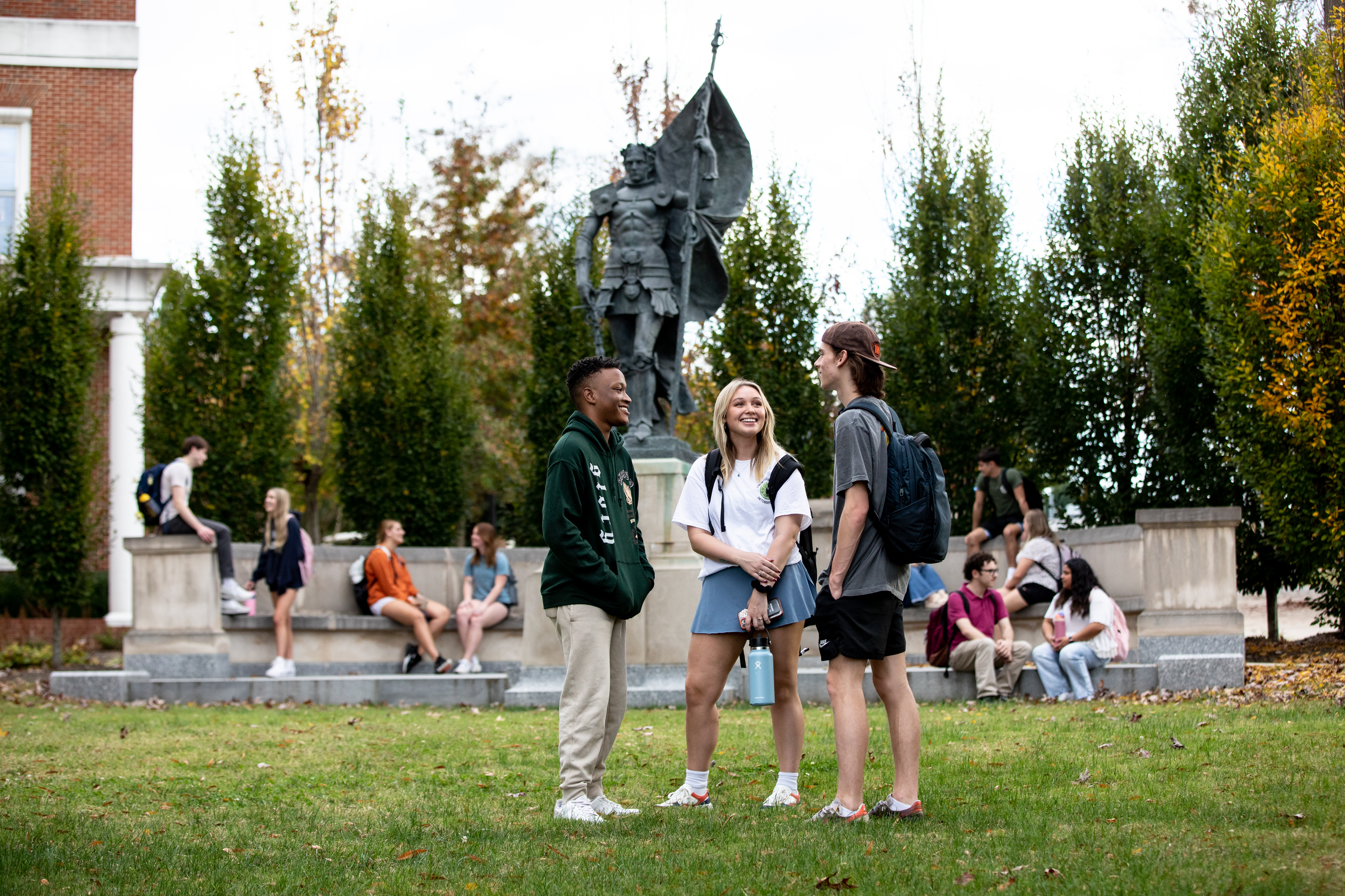 Students gather on the lawn and around the base of the Joan of Arc statue located at the south end of campus