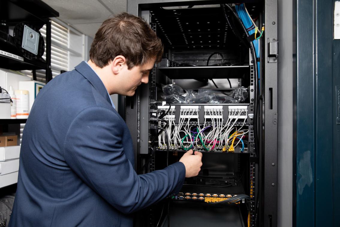 Master of Science in Information Technology student adjusts cables inside a server rack in a Longwood technology workspace.